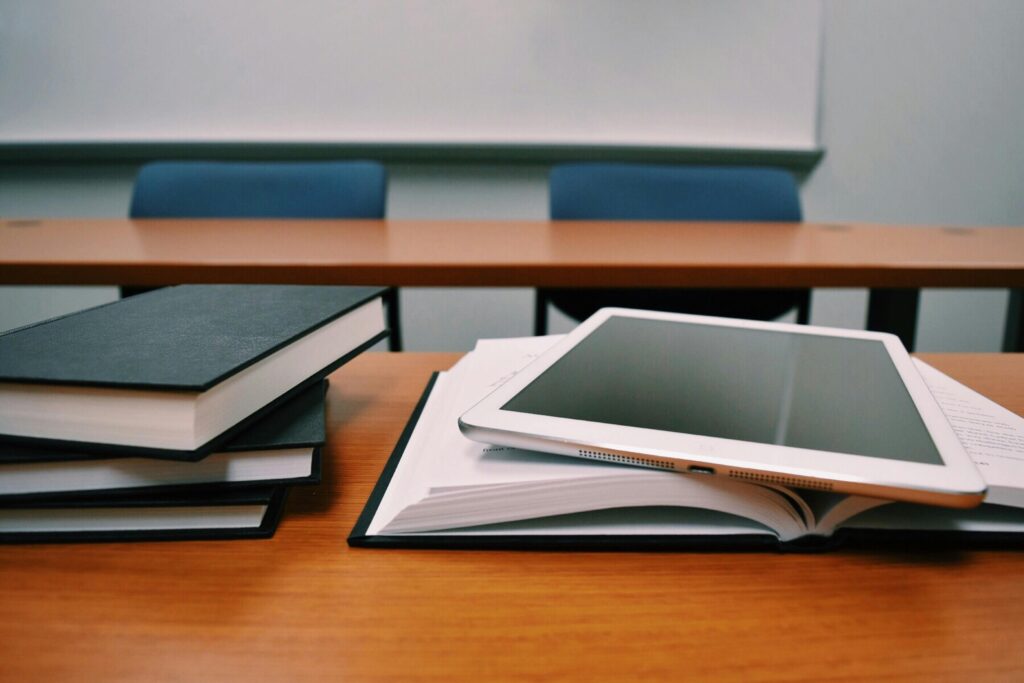 Stack of books on a desk with a tablet on top.